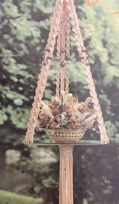 a bird feeder with beads hanging from it's sides and trees in the background