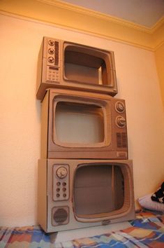 three microwaves stacked on top of each other in a room with a bed and wall