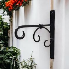 a black wrought iron hook on the side of a white wall with flowers in the background