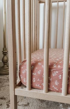 a baby crib with pink and white flowers on the bedding, next to a wooden rocking chair