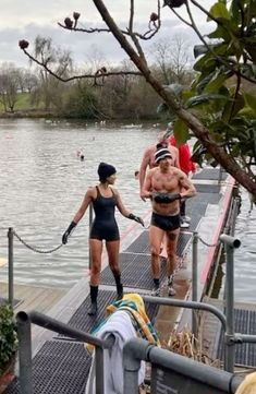 two women in bathing suits are walking on a dock near the water while others watch