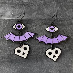 I designed these earrings with three levels of spookiness: eye, bat wing, and skull heart. 1.5 inch wide x 1.75 inch tall (49mm wide x 45mm tall) See coin photo for scale reference. Available in 2 color ways: Dark gray & white (does not glow), OR ✶Glow-in-the-dark✶ purple & white (the heart charm does not glow). The photo shows black ear hooks, but I'm now selling this with hypoallergenic steel ear hooks (perfect for sensitive ears). Modeled by Jaimee (in black), @soda_fontaine on Instag Black Earrings For Halloween Cosplay, Black Halloween Cosplay Earrings, Emo Metal Earrings For Halloween, Black Gothic Earrings For Cosplay, Edgy Pierced Halloween Earrings, Edgy Halloween Pierced Earrings, Edgy Pierced Earrings For Halloween, Witchy Halloween Earrings, Halloween Cosplay Earrings