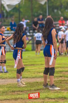 two girls in blue and orange uniforms standing on a field with their arms around each other