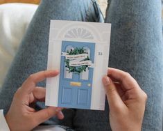 a person holding up a card with a blue door and wreath on the front cover