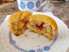 a half eaten muffin sitting on top of a white plate next to a cup