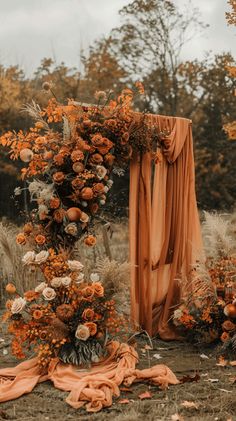 an outdoor ceremony with orange flowers and draping draped over the altar, surrounded by dry grass