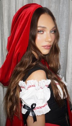 a woman with long brown hair wearing a red cape over her head and black dress