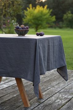 a bowl of fruit on top of a wooden table in the middle of a field