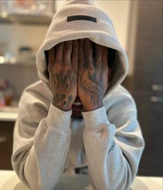 a person sitting at a table with their hands covering their face and both are covered by hoodies