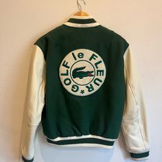 a green and white jacket with an alligator on it hanging from a hook against a wall