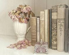 a white vase filled with pink flowers next to books