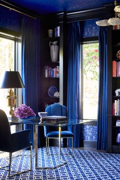 a living room with blue walls and curtains on the window sill, two chairs in front of a glass table