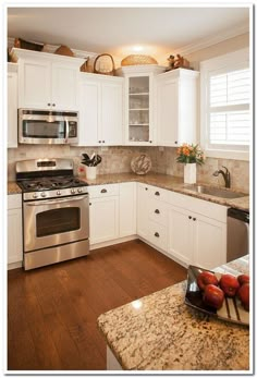 a kitchen with white cabinets and granite counter tops, stainless steel appliances and wooden floors