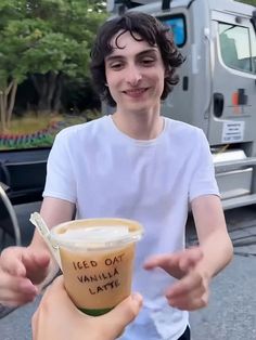 a young man holding up a cup of coffee in front of a truck with the words iced oat vanilla latte on it