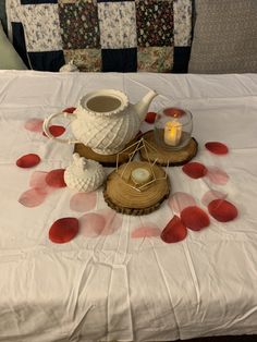 a table topped with a white tea pot next to a candle and some red petals