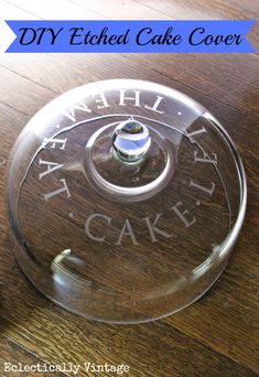 a clear cake cover sitting on top of a wooden table next to a cupcake