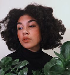 a close up of a person with curly hair and green plants in front of her