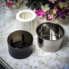 two metal bowls sitting next to each other on a table with flowers in the background