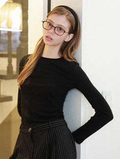 a young woman wearing glasses leaning against a wall with her hands on her hips and looking at the camera