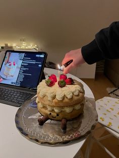 a cake with strawberries on top is being lit by someone using a laptop computer