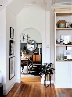 a dining room with white walls and wood flooring is seen through an arch in the wall