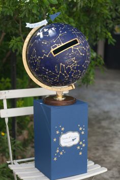 a blue and gold globe sitting on top of a wooden block in front of a tree