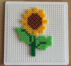 a flower made out of legos sitting on top of a white plate with green and yellow beads