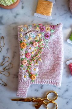 a pink sweater with flowers on it next to scissors and thread