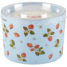 a blue tin with strawberries and flowers on the lid is sitting in front of a white background