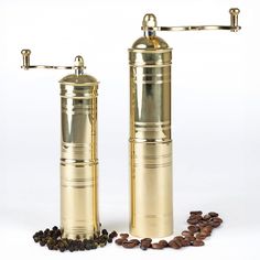 two gold coffee grinders next to some coffee beans