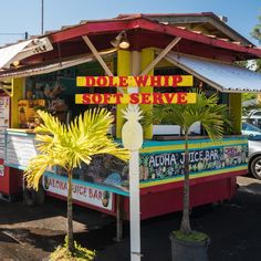 a colorful food stand with palm trees in the foreground and parked cars behind it