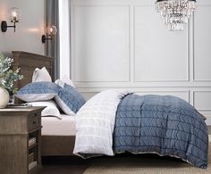 a bed with blue and white comforter next to a night stand in a bedroom