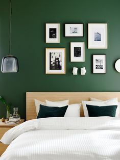 a bedroom with green walls and pictures on the wall above the bed, along with white linens