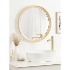 a white sink sitting under a round mirror on top of a counter next to a vase