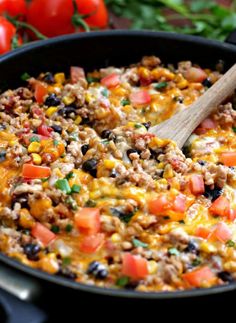 a skillet filled with taco salad and topped with a wooden spoon next to tomatoes