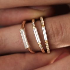 two gold rings with white stones on each one and diamonds on the other, in front of a woman's hand