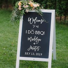 a welcome sign with flowers and greenery on it in front of some trees at a wedding