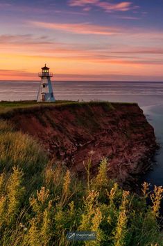 a light house sitting on top of a cliff next to the ocean under a colorful sky