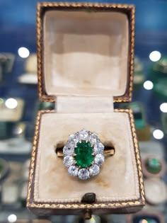 an emerald and diamond ring sits in a box on display at a jewelery shop