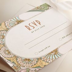 a close up of a wedding card on a white surface with flowers and leaves around it