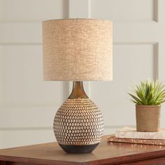 a table lamp sitting on top of a wooden table next to a potted plant