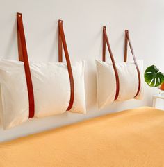 three pillows hanging on the wall above a bed with white sheets and brown leather straps