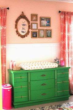 a baby's room with pink walls, green dresser and pictures on the wall