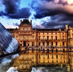 an old building with a large glass pyramid in front of it on a cloudy day