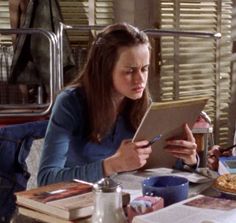 two women are sitting at a table with pizza and drinks in front of them, looking at something on the tablet