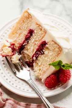 a slice of cake with white frosting and raspberries on a plate next to a fork