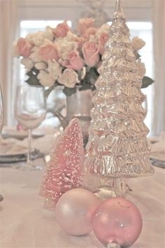 the table is set with pink and white ornaments, silver vases, and roses