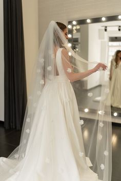 a woman in a wedding dress looking at herself in the mirror with her veil pulled back