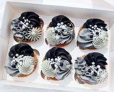 six cupcakes in a white box with black and grey frosting on them