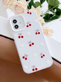 an iphone case with red cherries and white daisies on it sitting next to flowers